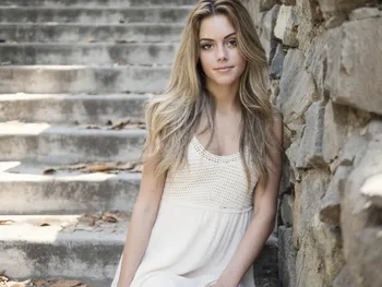 An AI-generated image of a young woman with blonde hair sitting on stone steps.
