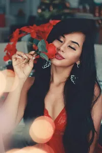 A beautiful woman with dark hair holding a single red rose to her face, symbolizing romance.